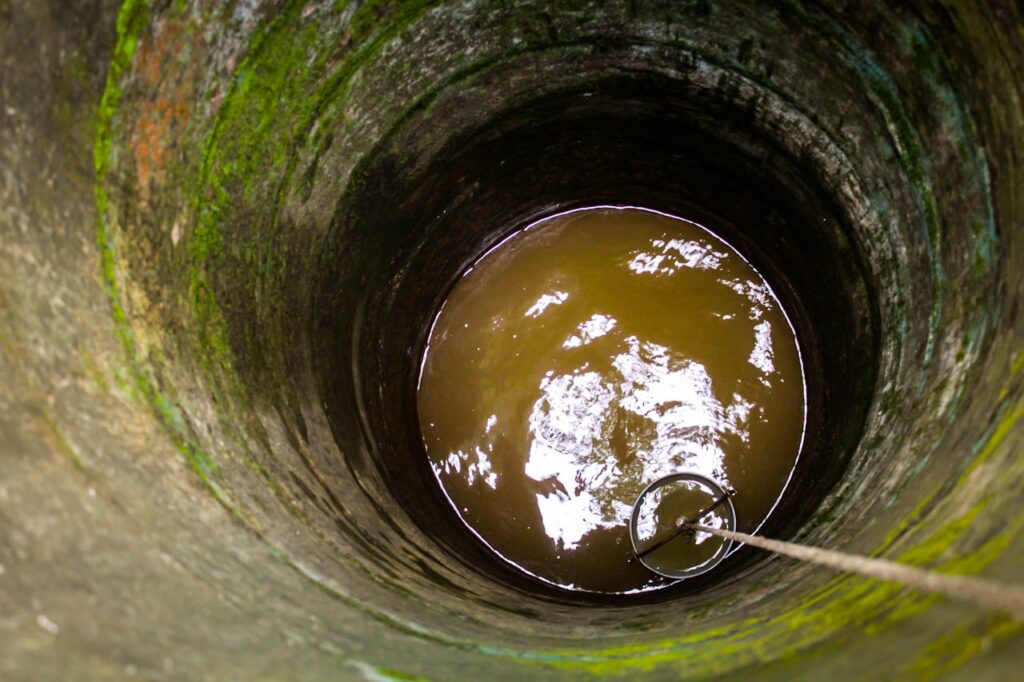 A view down an old stone well showing murky water and a rope with a bucket.